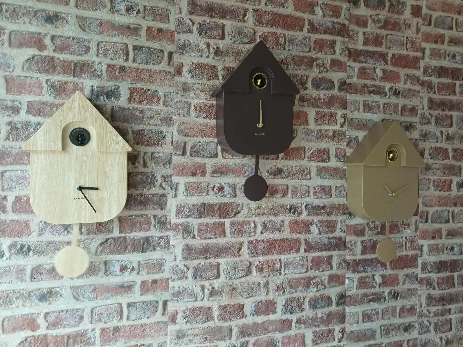 Trois horloges coucou Karlsson accrochées au mur de briques de la boutique