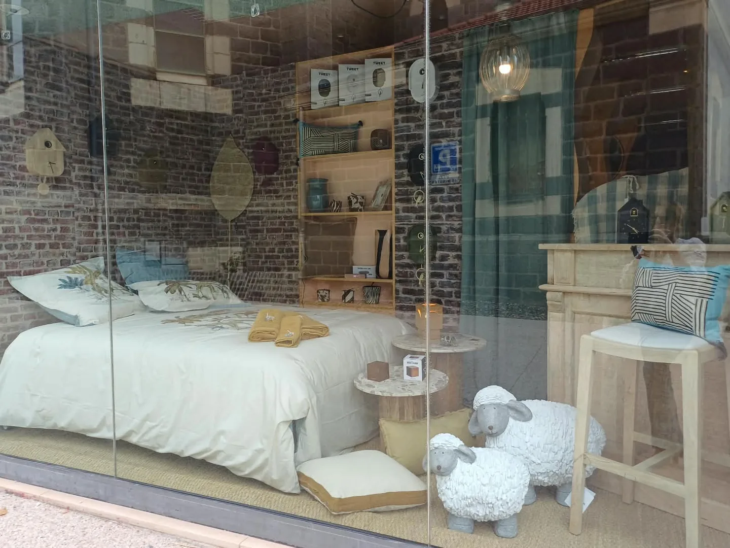 La nouvelle vitrine de septembre : lit habillé d'une housse Sylvie Thiriez à motif savane, mur de briques, horloges coucou et moutons